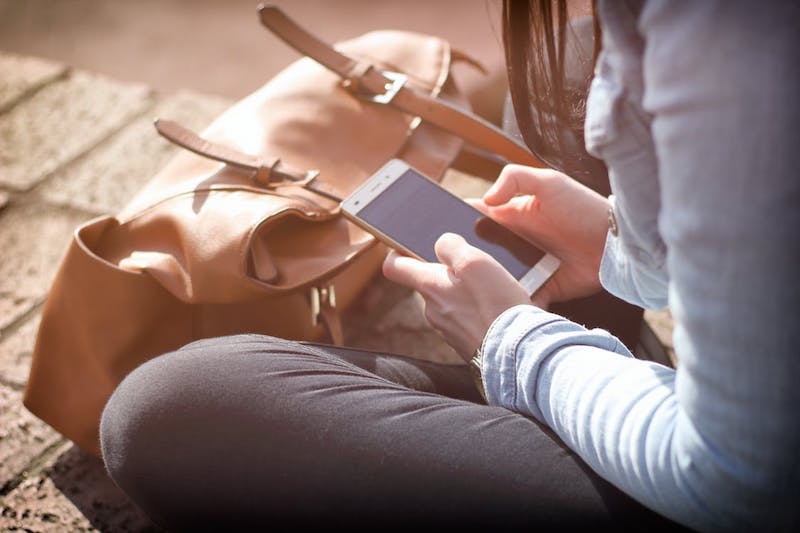 Woman sitting on ground staring down at phone, image used for Ari Monkarsh blog on why we should look at phones less