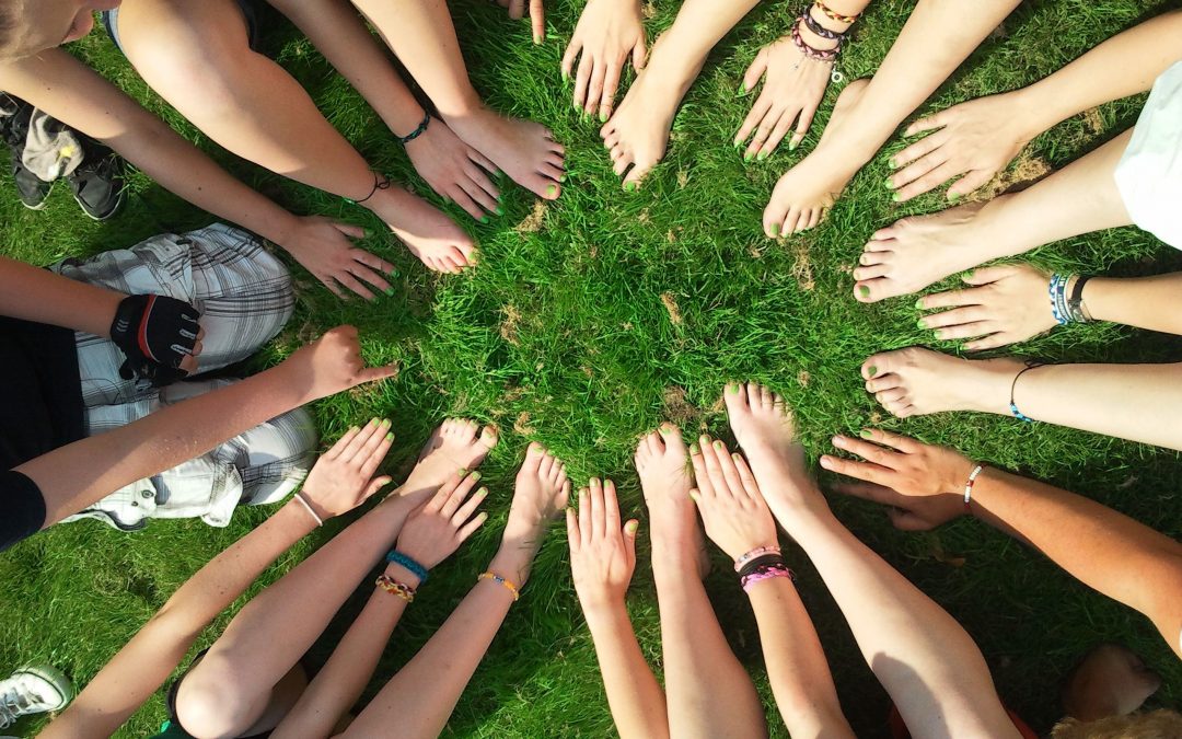 Group of people sitting in a circle in the grass with their hands and feet toward each other, image used for Ari Monkarsh blog about how to keep a team motivated